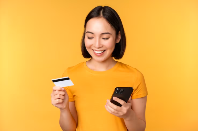 A woman with short hair holding a credit card and a phone.