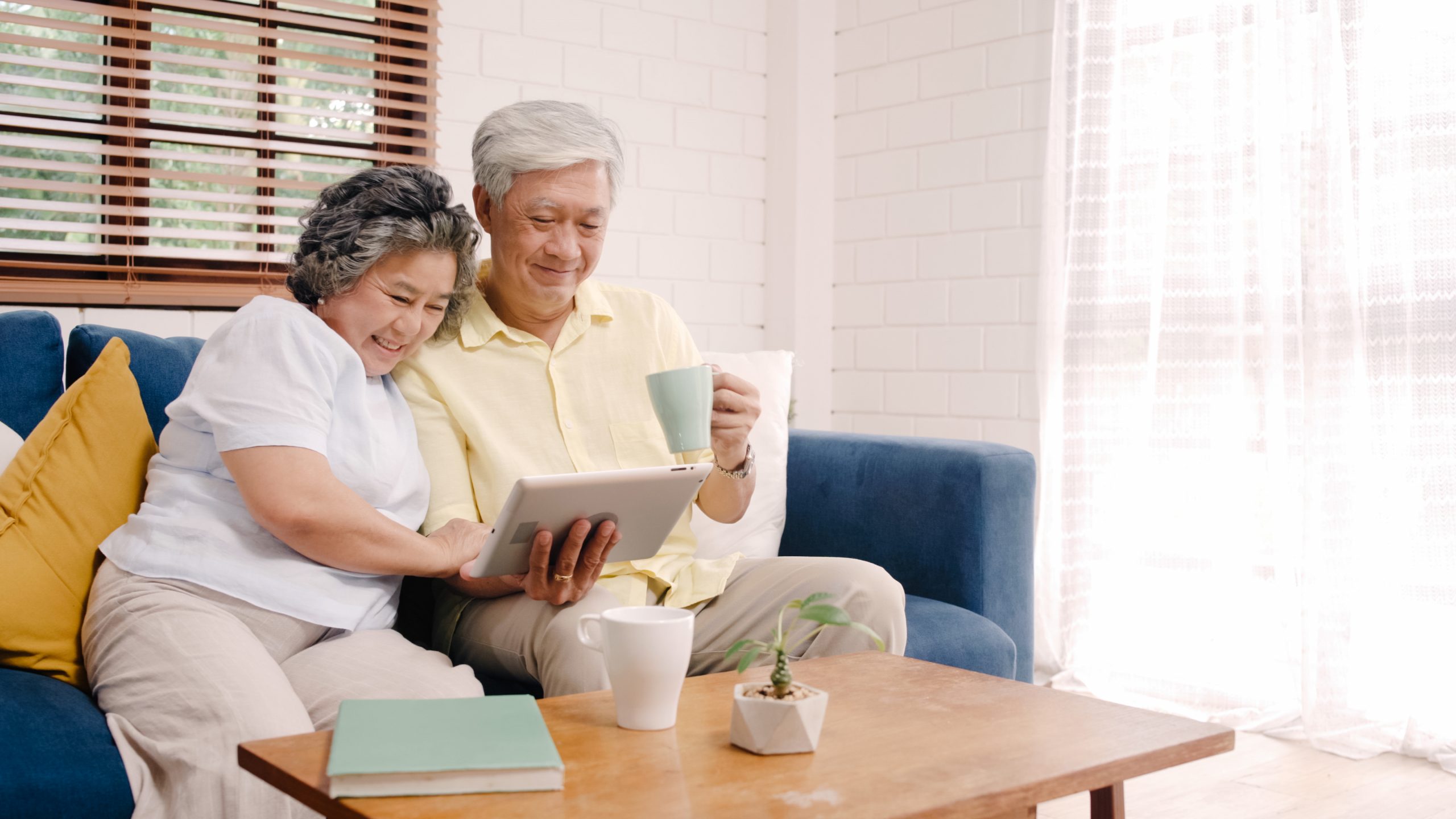 elderly asian couple looking at a tablet while having coffee