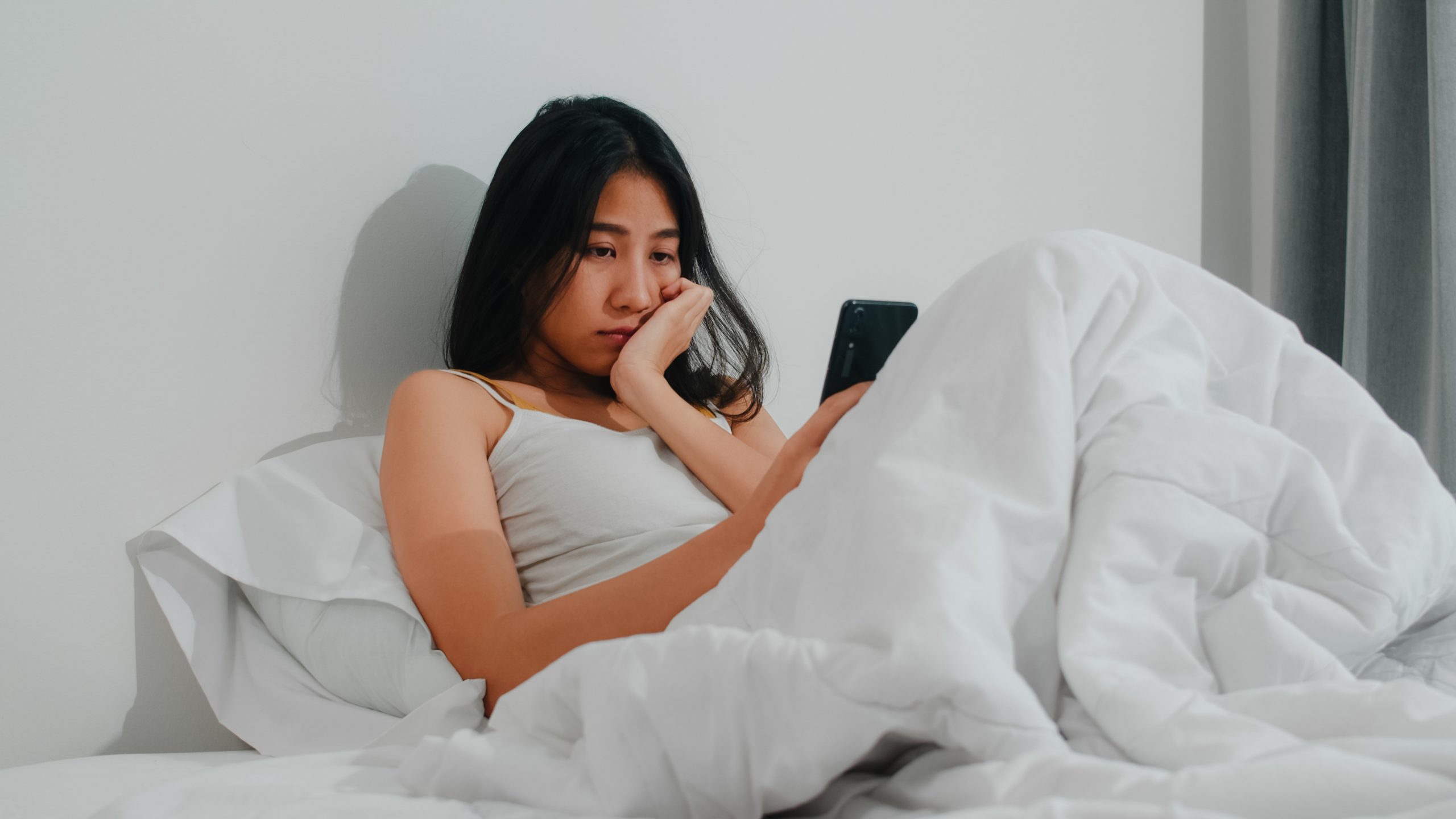 Young Asian woman using smartphone in bed.