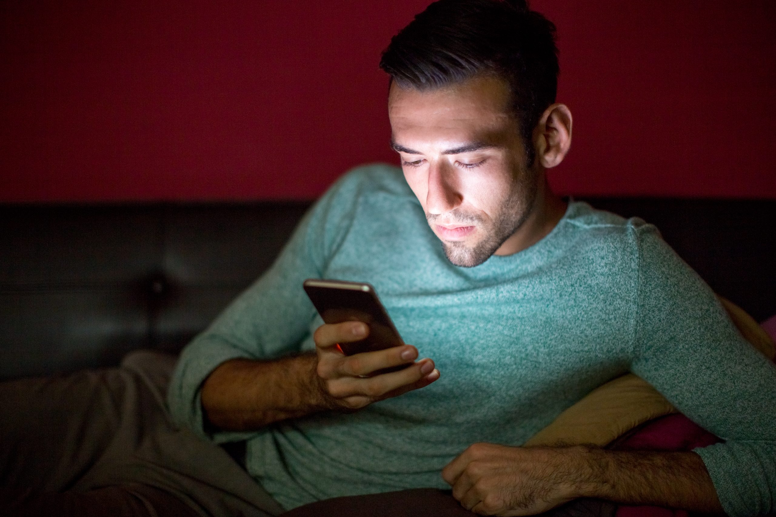 Serious man using smartphone on sofa at night.