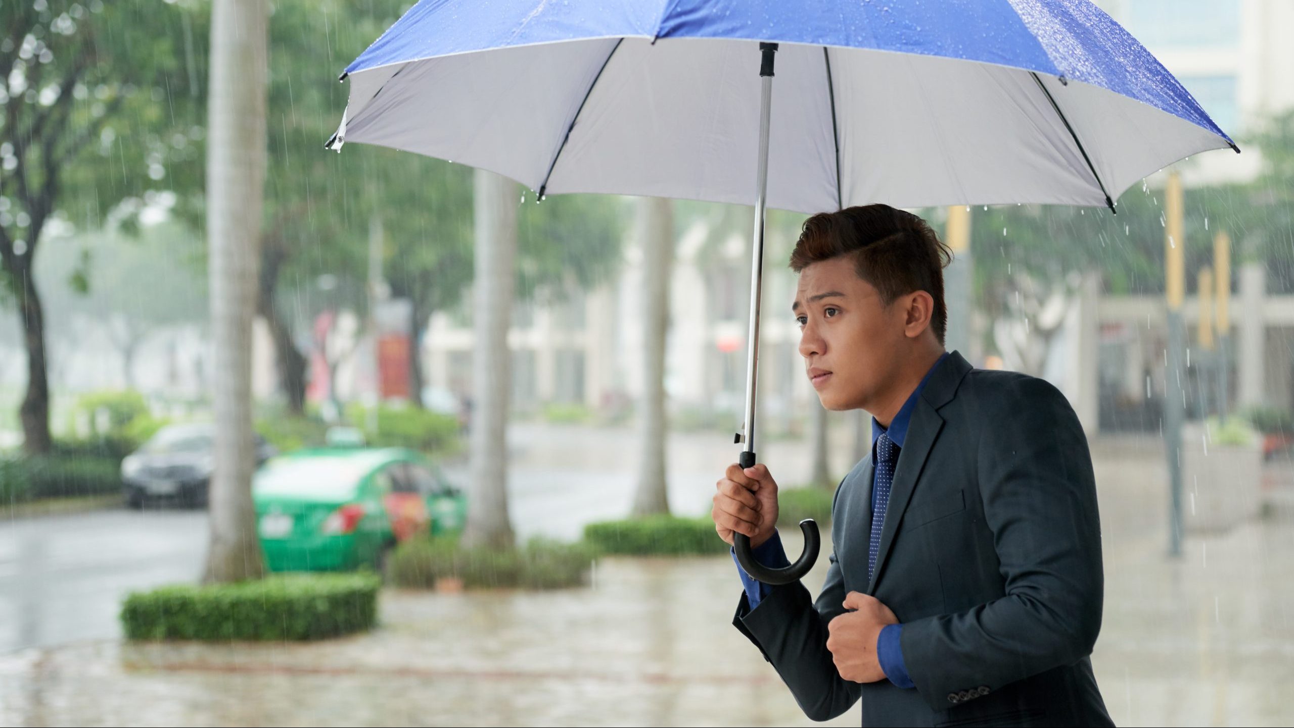 Man in a business suit holding an umbrella in rainy weather.