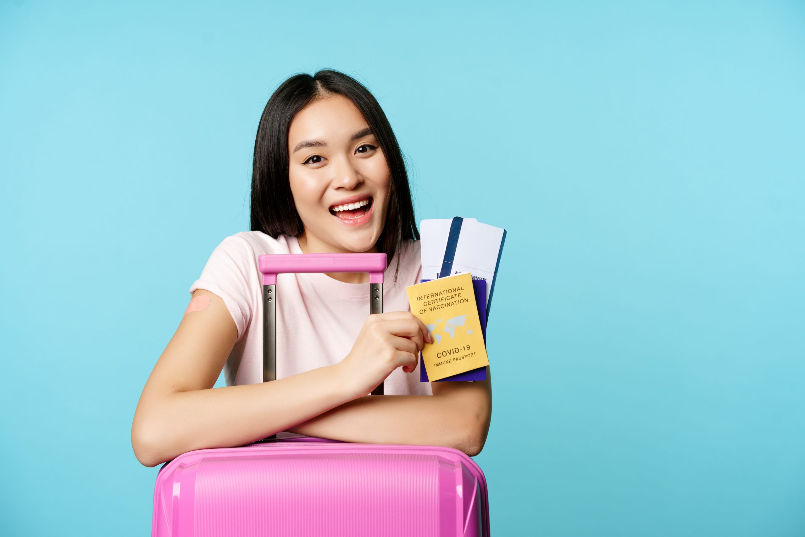 Asian girl hugging her pink luggage while holding her plane ticket and passport.