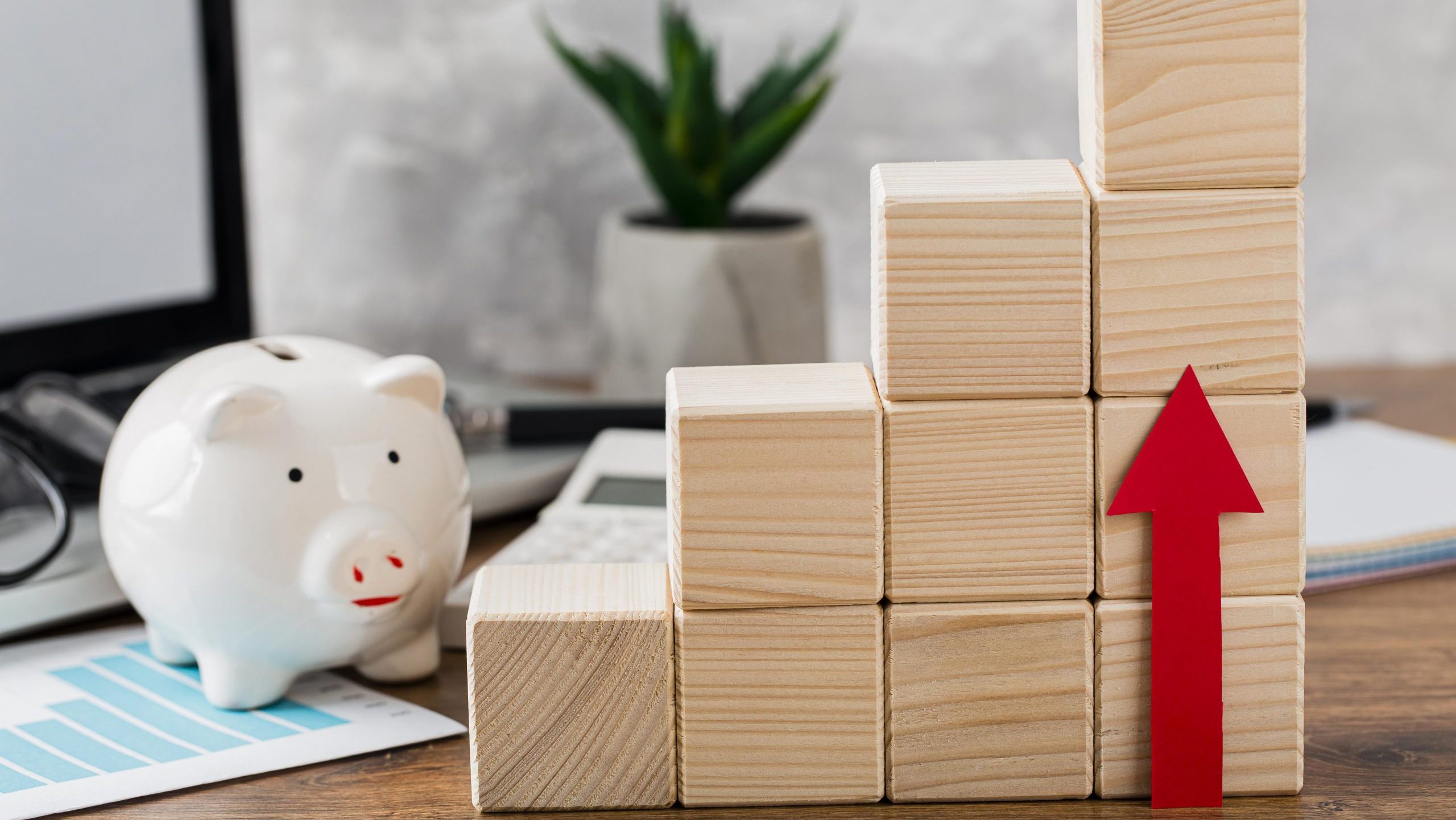 A piggy bank and wooden blocks with red arrow on a table.