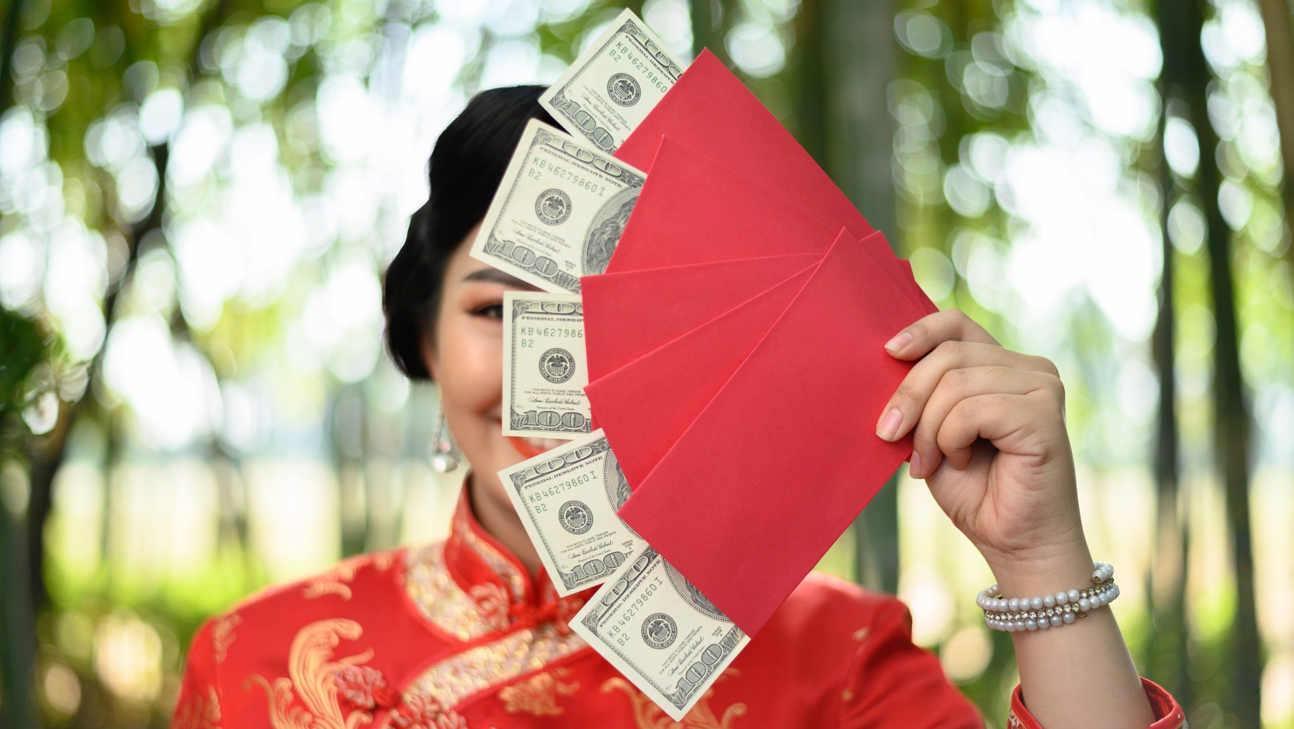 Asian woman in red holding red envelopes with money.