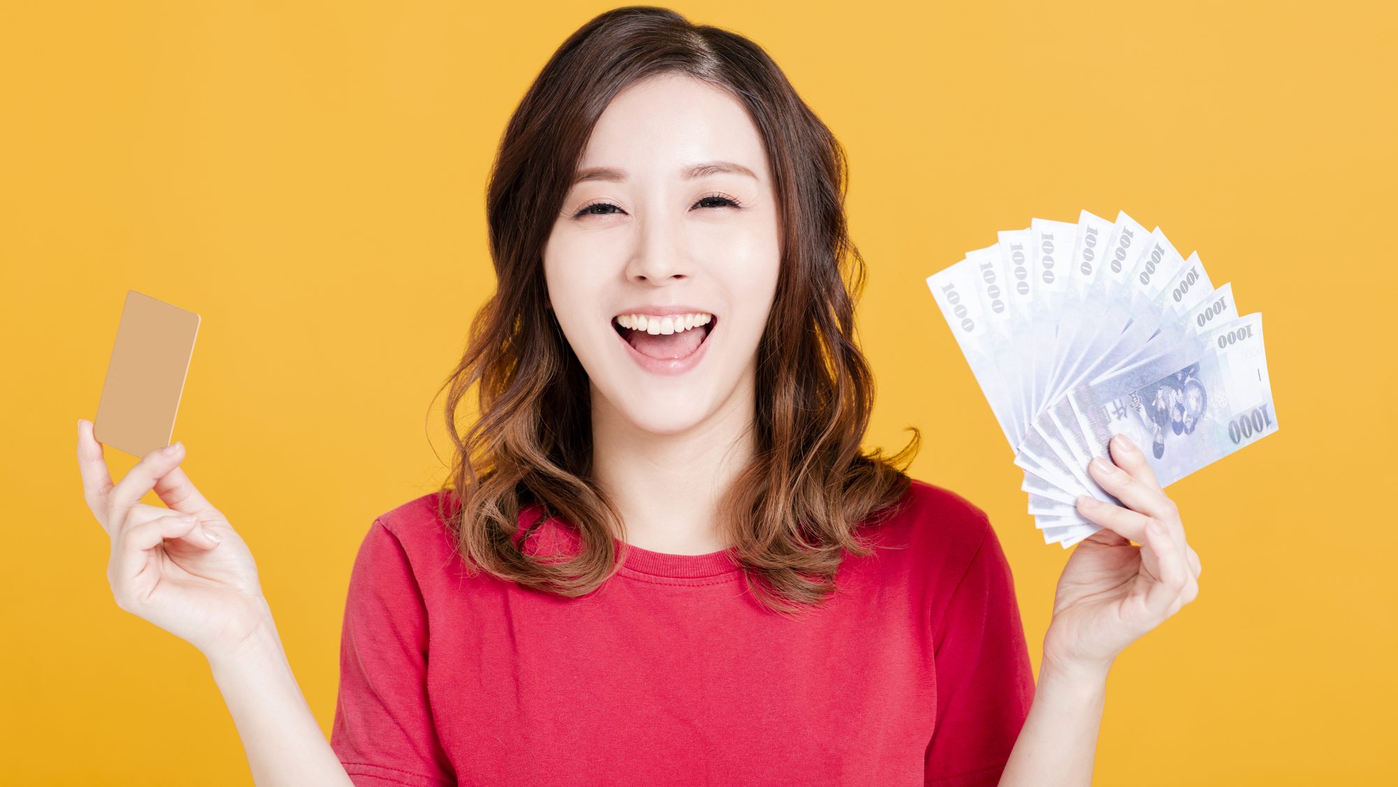 Happy young woman holding money and credit card.