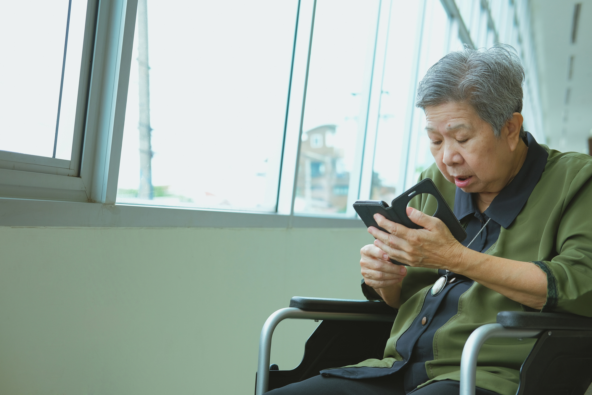 Elder woman in wheelchair holding mobile phone.