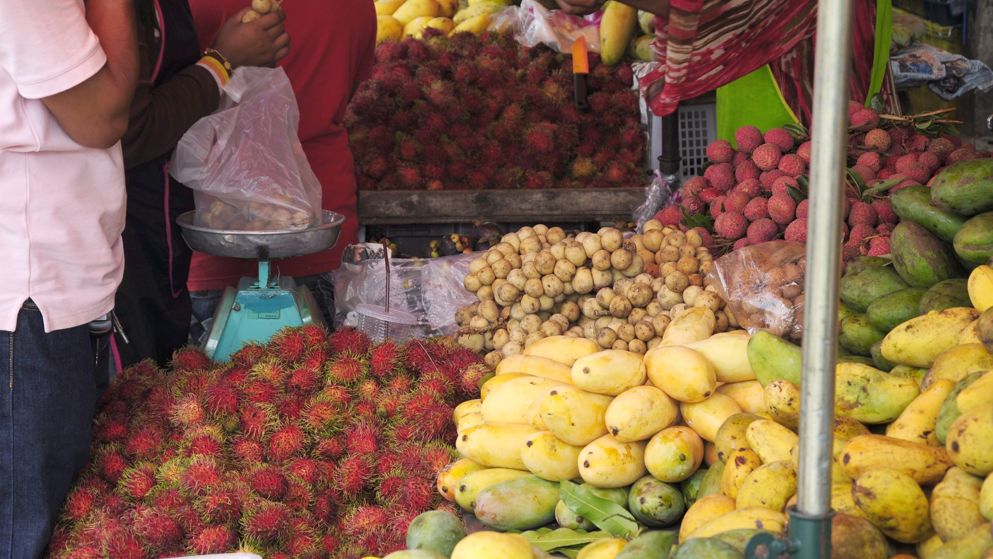 People buying fruits from a fruit vendor in the market.