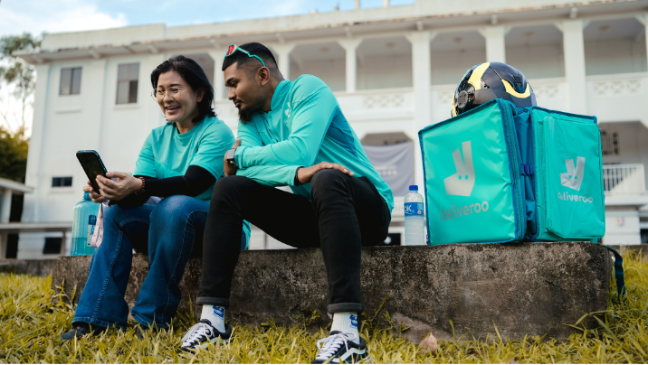 Deliveroo man and woman looking at a phone smiling.