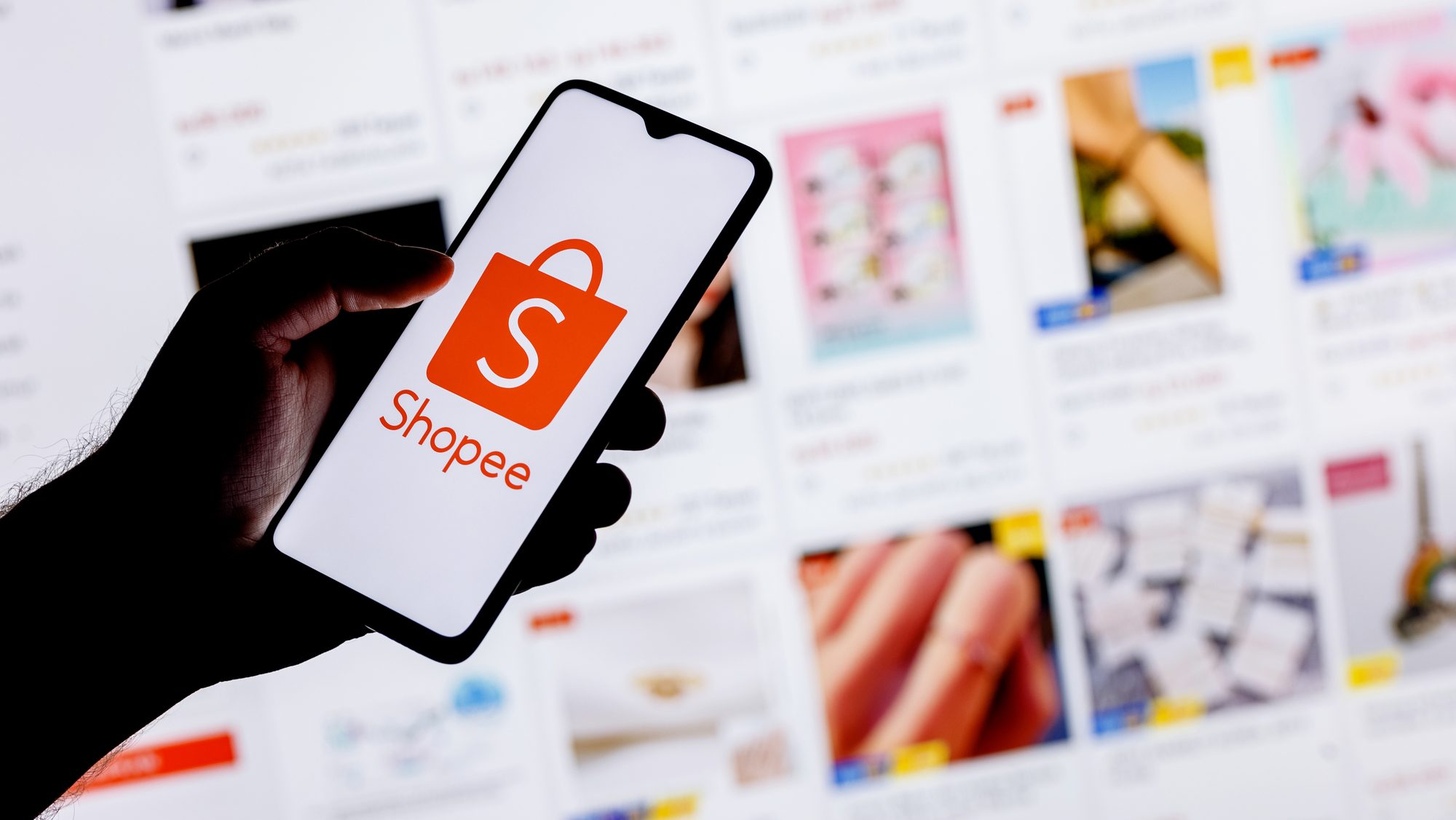 Hand holding phone with Shopee logo on screen.
